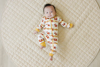 Baby wearing GOTS certified organic cotton zip romper with Aztec pony print, lying on quilted mat. Chemical-free safety.