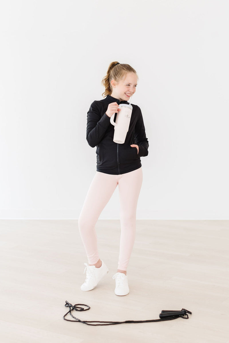 A girl wearing Zen Pink Active Legging by Mila & Rose, holding a beige water bottle and standing confidently in a white room, showcasing her active style.
