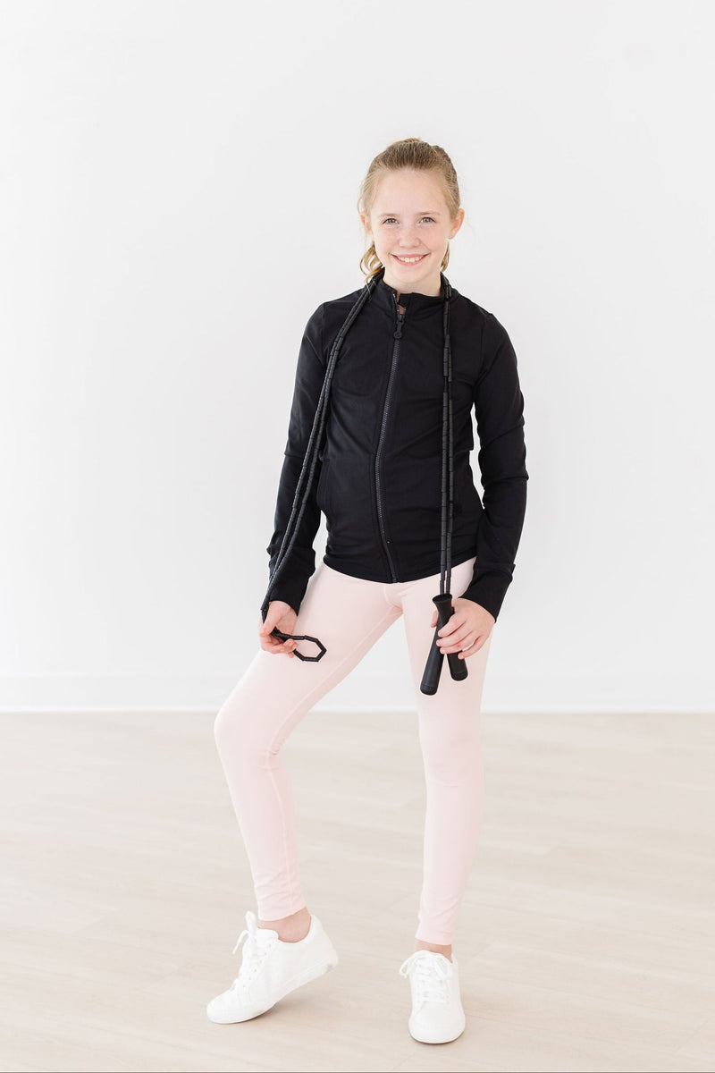 A girl sporting Zen Pink Active Legging by Mila & Rose, posed with a jump rope around her neck, smiling while dressed in a fashionable black jacket.