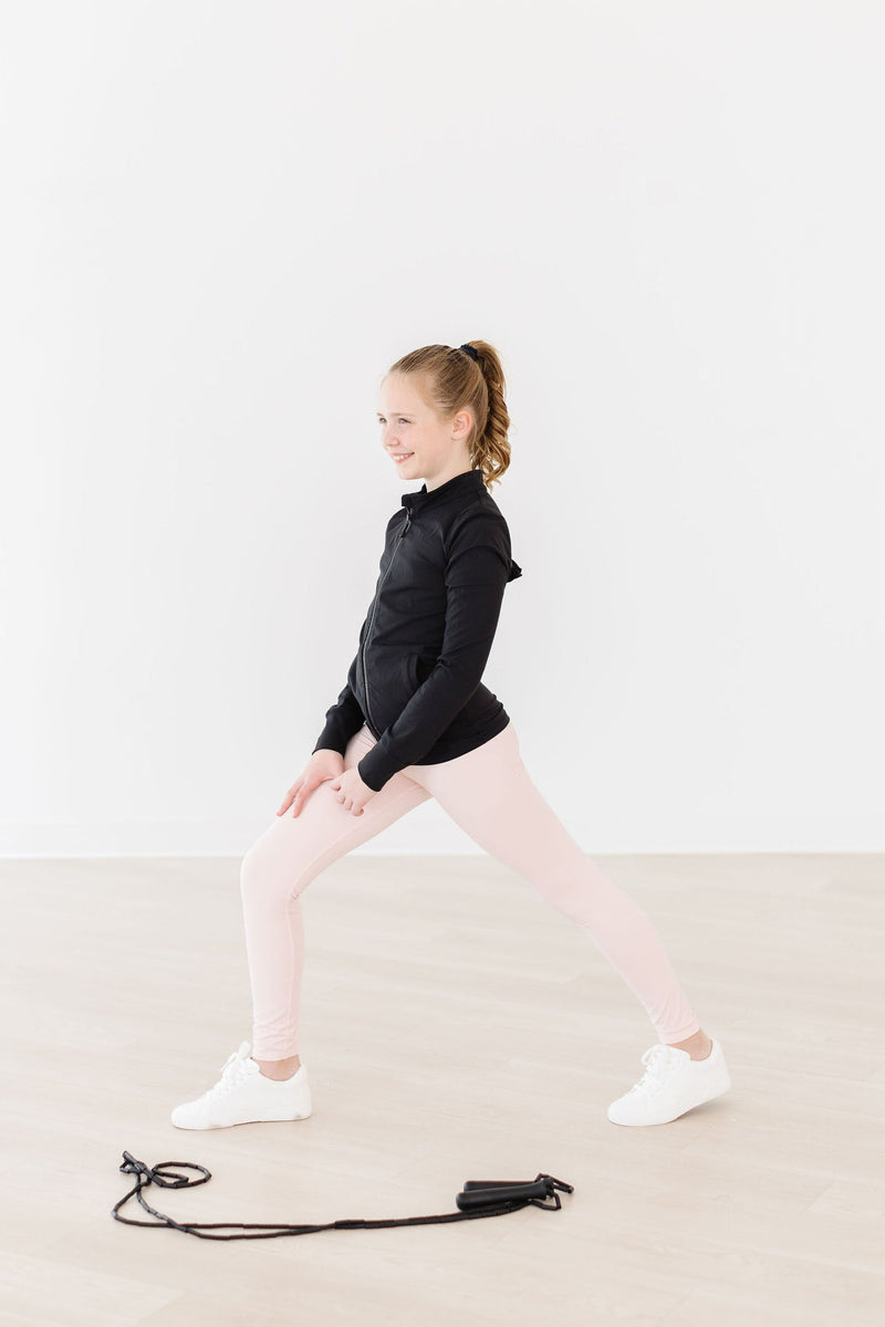 A girl demonstrating a lunge in Zen Pink Active Legging by Mila & Rose, wearing a black jacket, exuding a playful and active spirit in a bright room.