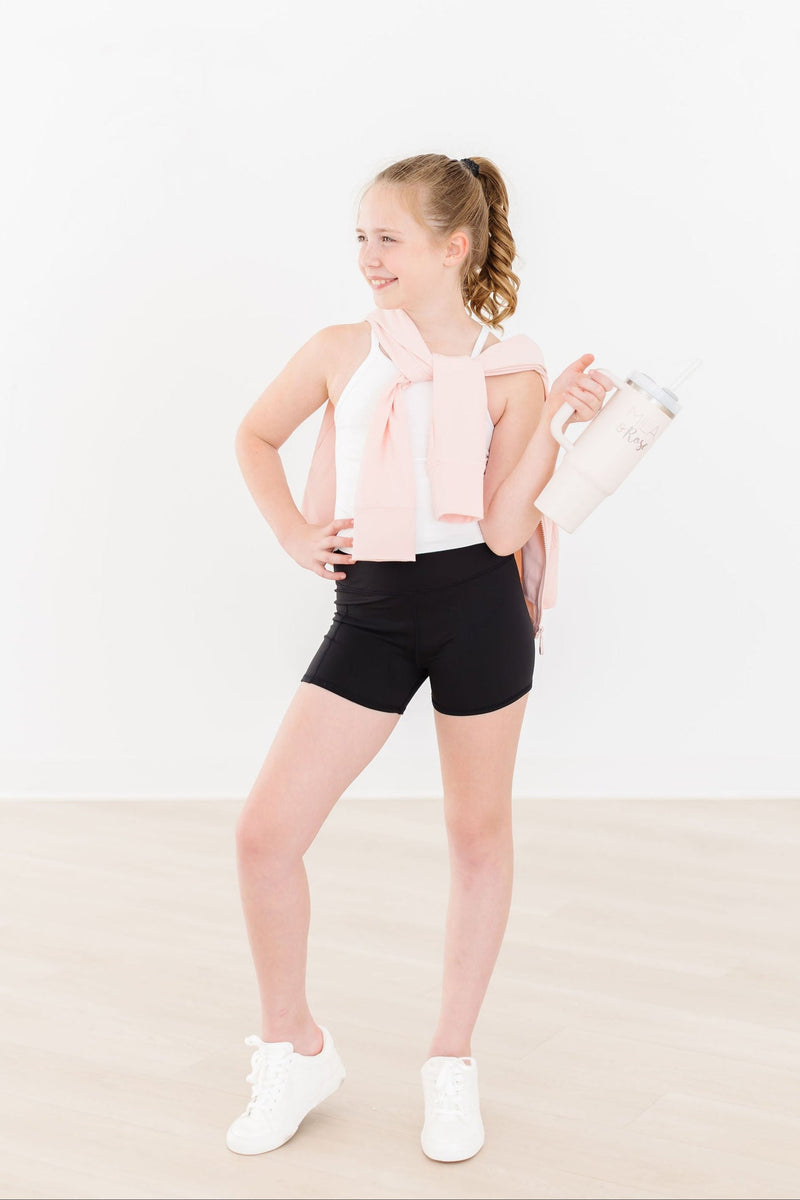 Girl posing with hands on hips, wearing the Zen Pink Full-Zip Ruffle Active Jacket over a tank top and black shorts, ready for any activity.