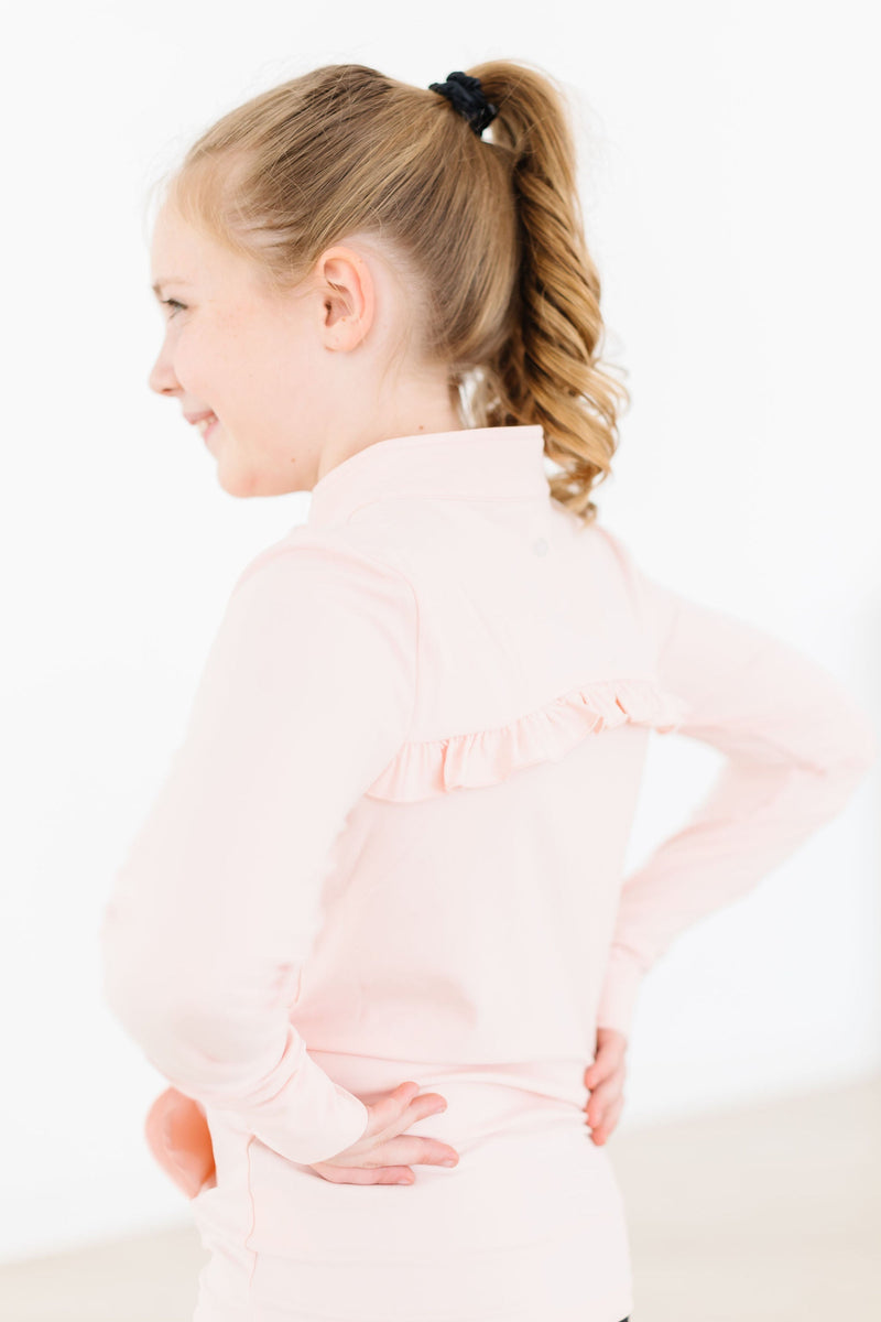 A smiling girl in a Zen Pink Full-Zip Ruffle Active Jacket from the back, highlighting the playful ruffle detail, as she poses with her hands on her hips, emphasizing comfort and style.