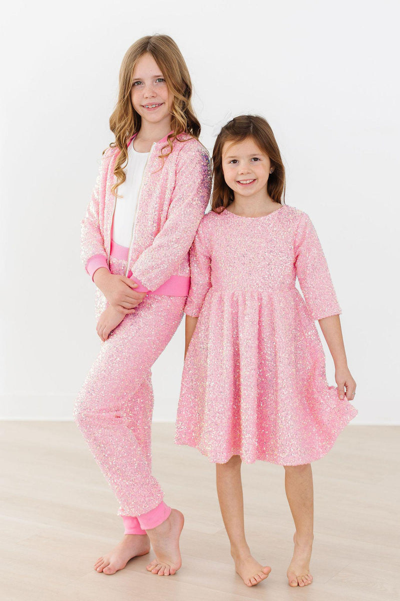 Two girls showcasing fashionable Bubblegum Pink Sequin Joggers by Mila & Rose ®, with one wearing a matching sequined jacket and the other in a stylish pink dress, perfect for parties and casual outings.