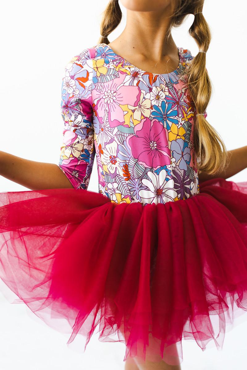 Girl in a Mauve What's Up Buttercup 3/4 Tutu Leotard with a vibrant floral design, showcasing a fluffy maroon tutu, perfect for dance and play.