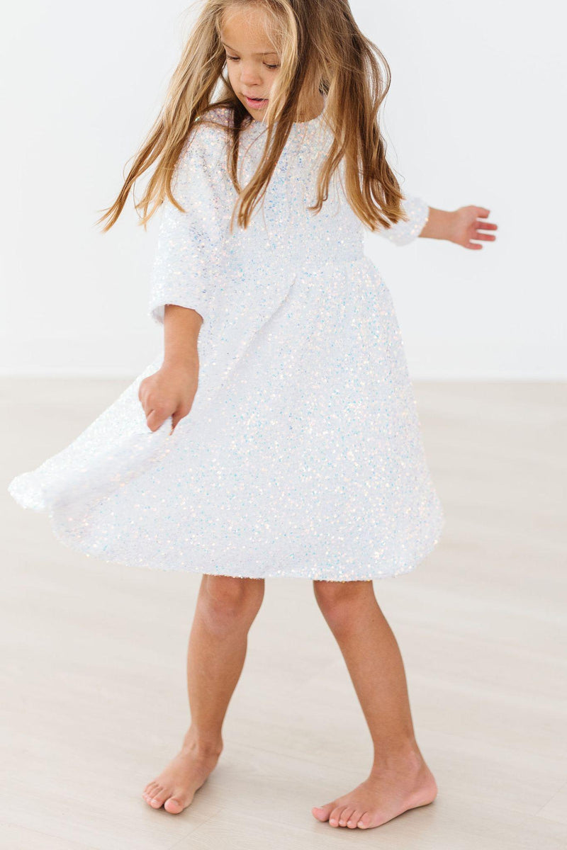 A girl in a white sequin party dress spinning joyfully, highlighting the dress's flow and sparkling sequins.