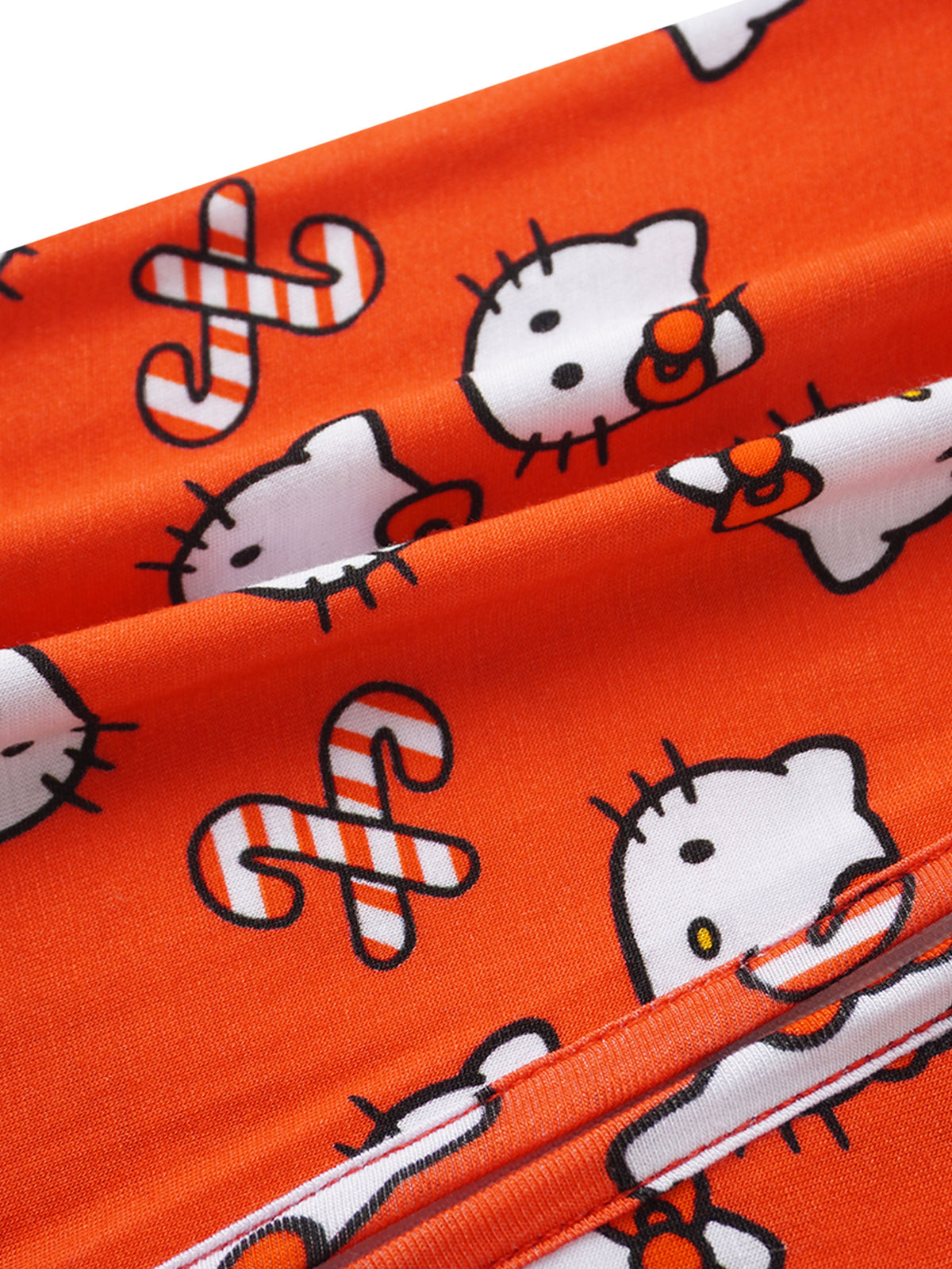 Vibrant orange fabric macro shot with repeating Hello Kitty faces, red bows, and detailed stitching.