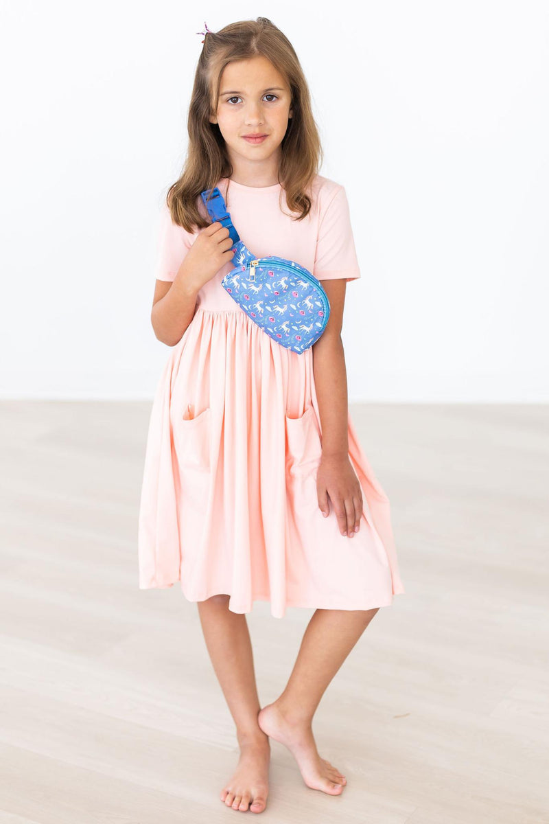 Stylish girl wearing a Peach S/S Pocket Twirl Dress by Mila & Rose, holding a blue patterned bag, showcasing the dress's versatility and chic appeal.