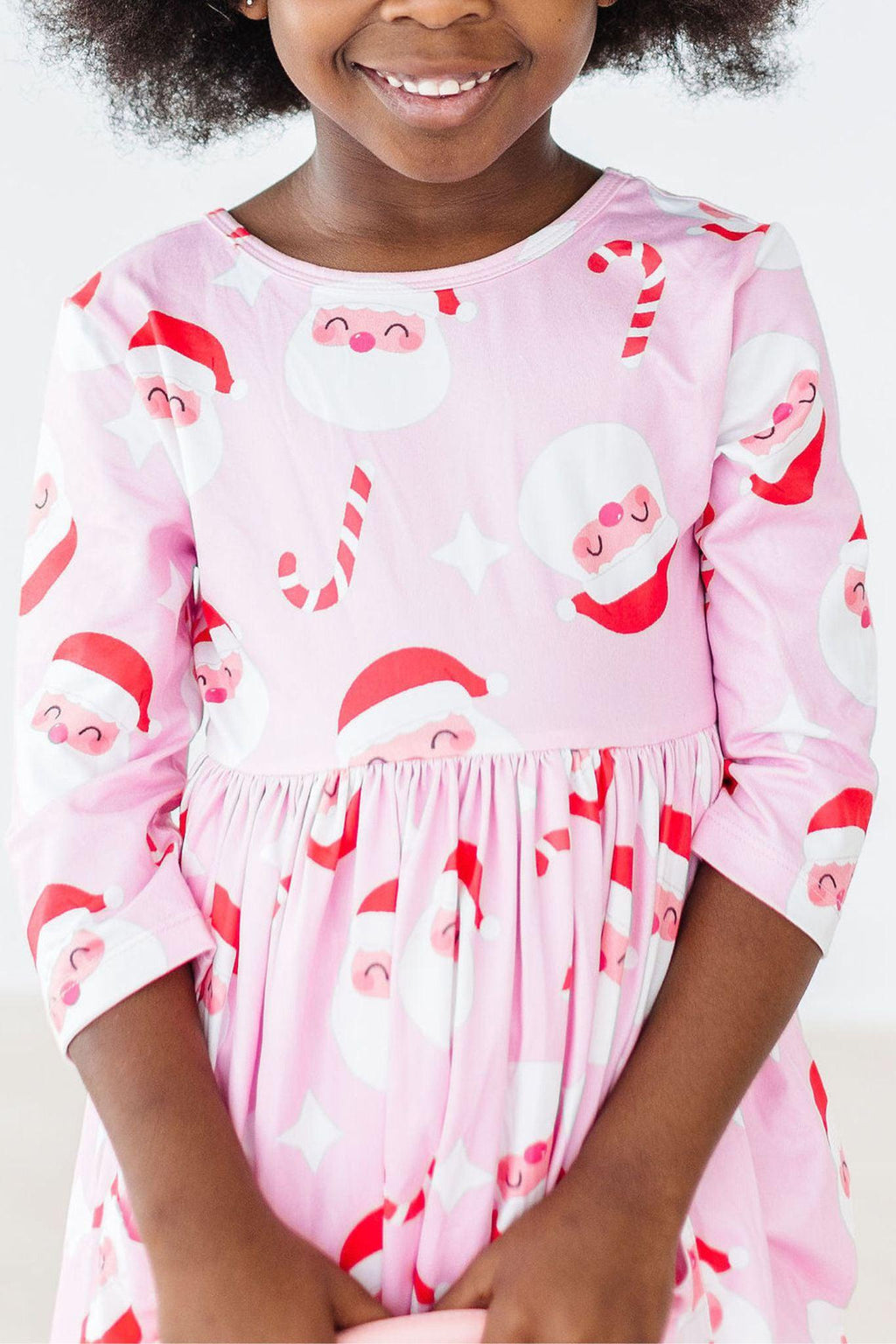 Jingle Bells 3/4 Sleeve Pocket Twirl Dress featuring a joyful design with Santa and candy canes, worn by a smiling girl with curly hair, perfect for festive occasions.