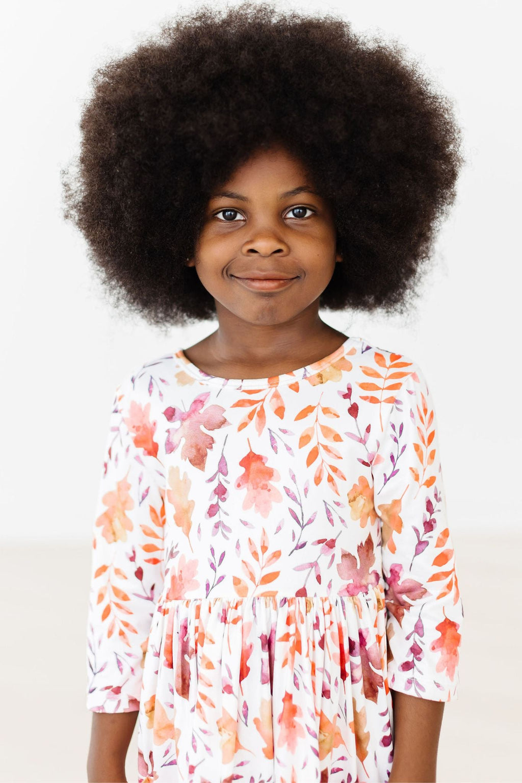 Happy girl wearing the Falling Leaves 3/4 Sleeve Pocket Twirl Dress by Mila & Rose, showcasing lively autumn colors and a beautiful twirl-ready skirt.