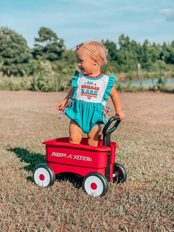 Turquoise cotton All American baby romper with white bib and red text worn by toddler outdoors