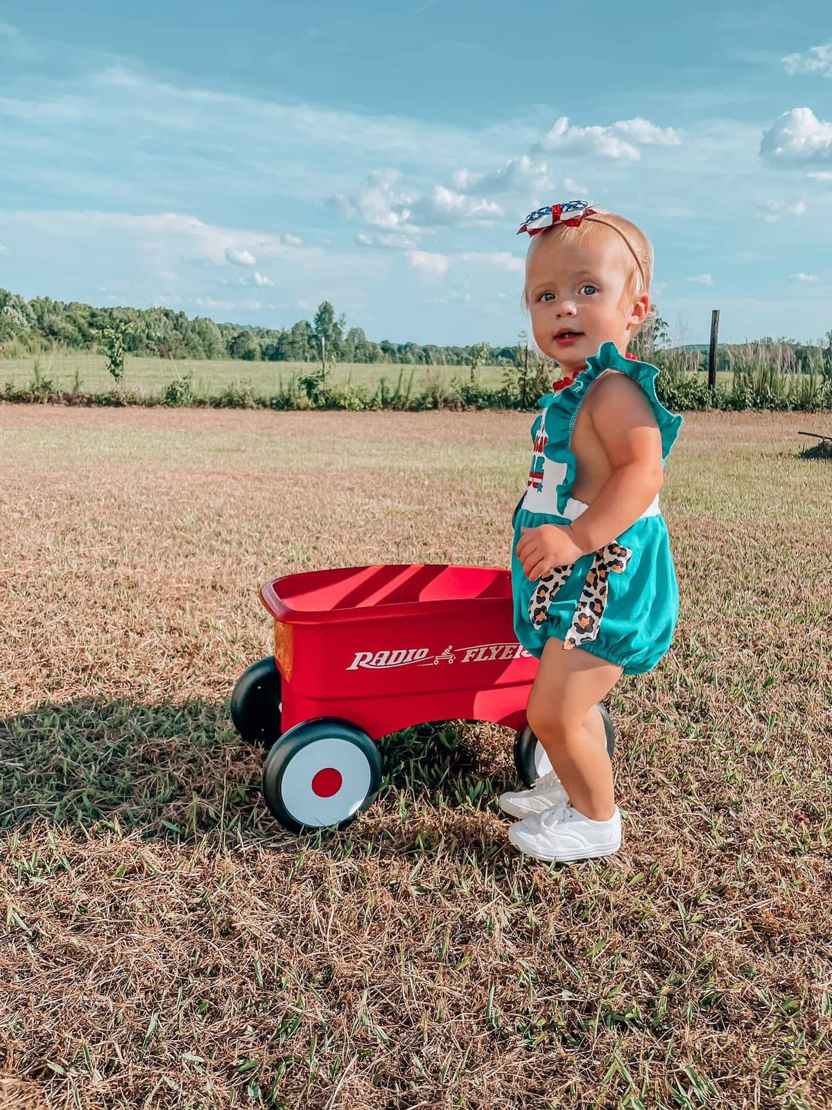 Toddler wearing teal cotton All American baby romper with ruffles and leopard print accents outdoors