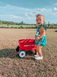 Toddler wearing teal cotton All American baby romper with ruffles and leopard print accents outdoors