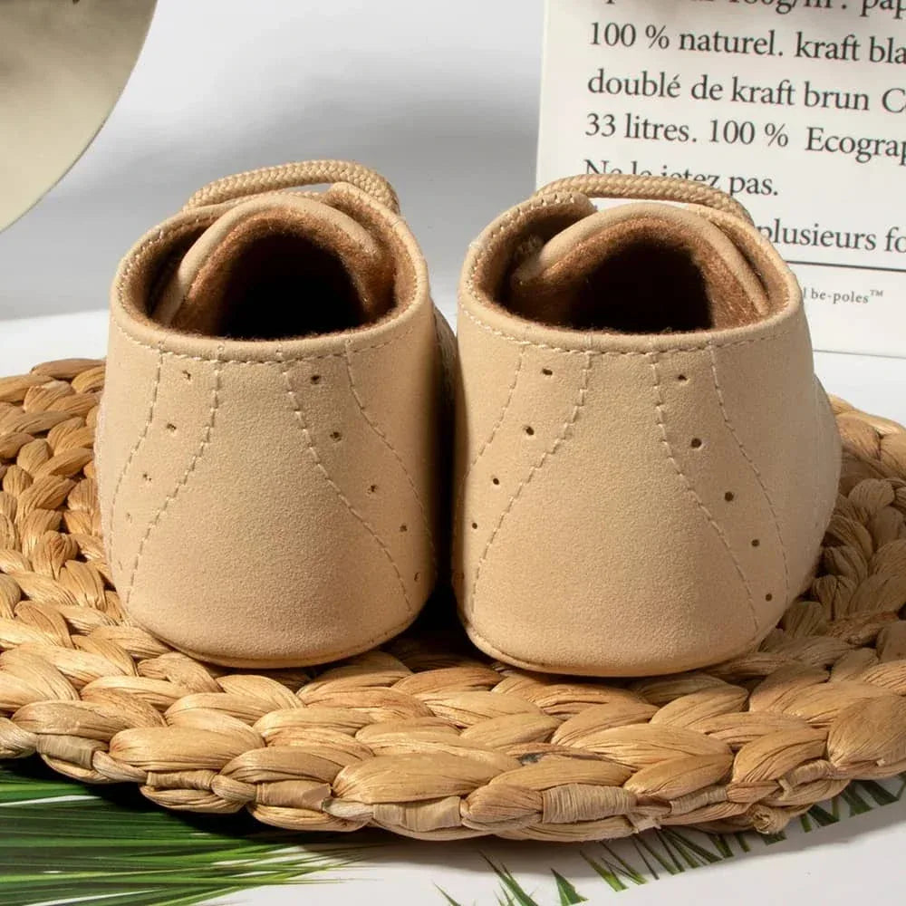 Pair of beige anti-slip baby shoes for boys in newborn size shown from the back on a woven mat