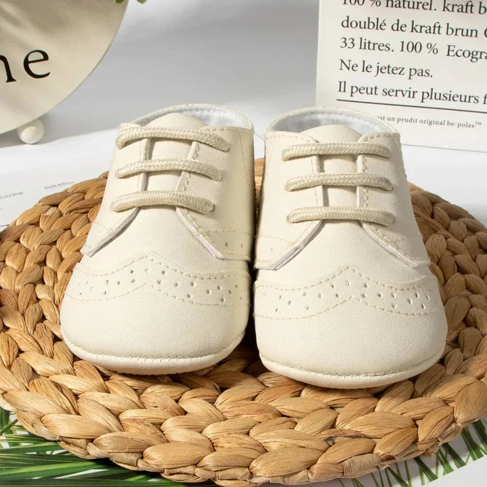 Cream-colored anti-slip baby shoes for boys in newborn size displayed on woven mat