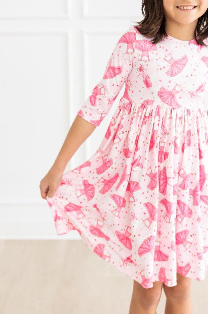 Girl wearing the Pirouette 3/4 Sleeve Pocket Twirl Dress with vibrant pink pattern, showcasing the dress's charming scoop back and playful skirt.