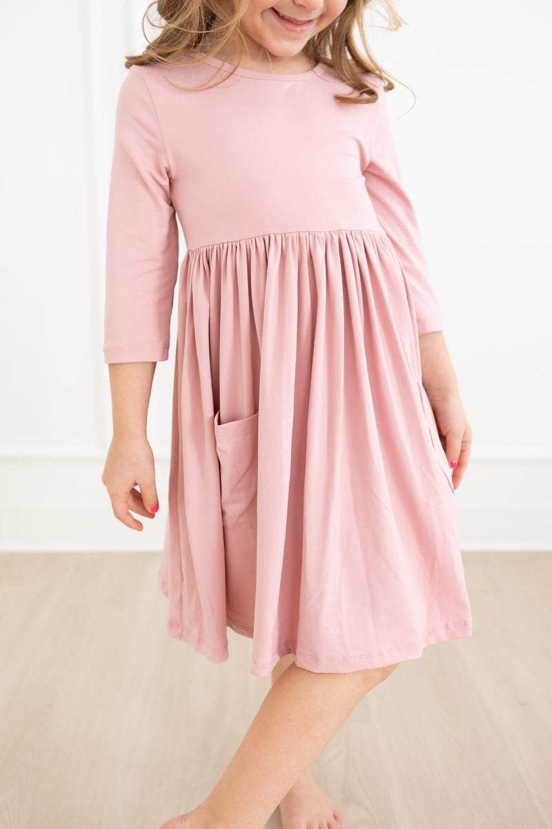 A young girl wearing the Vintage Pink 3/4 Sleeve Pocket Twirl Dress from Mila & Rose, smiling while twirling the dress, showcasing its playful design.