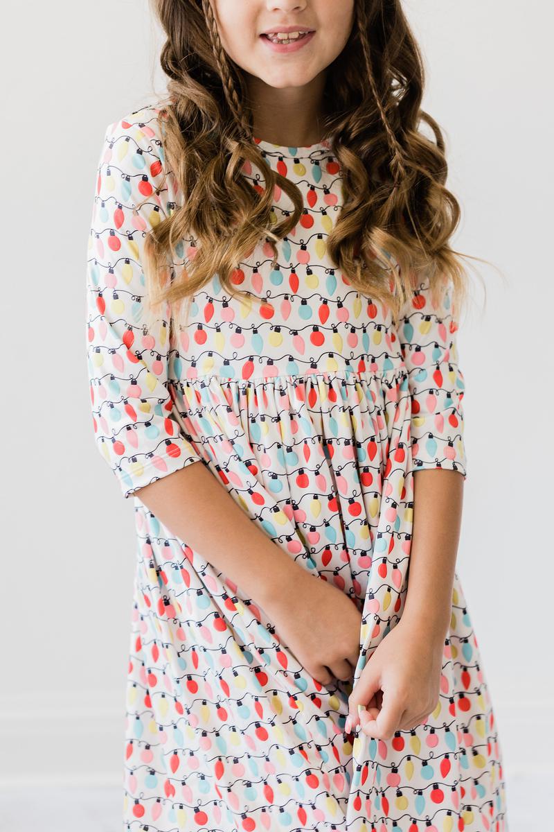 Child wearing the Merry & Bright 3/4 Sleeve Pocket Twirl Dress, featuring a colorful lights pattern, showcasing comfort and style for young girls.