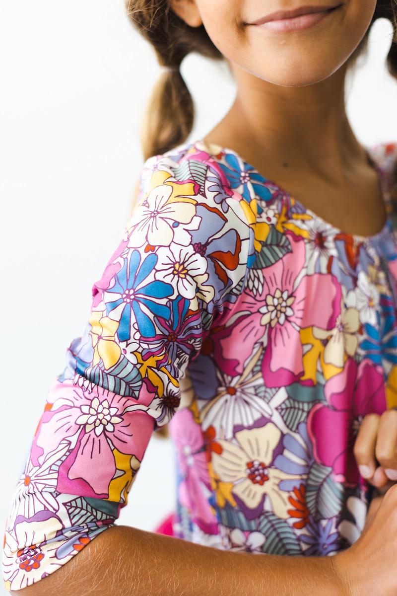 Close-up of a girl's smile while wearing a Mauve What's Up Buttercup 3/4 Tutu Leotard, featuring a detailed floral pattern that adds charm and style.