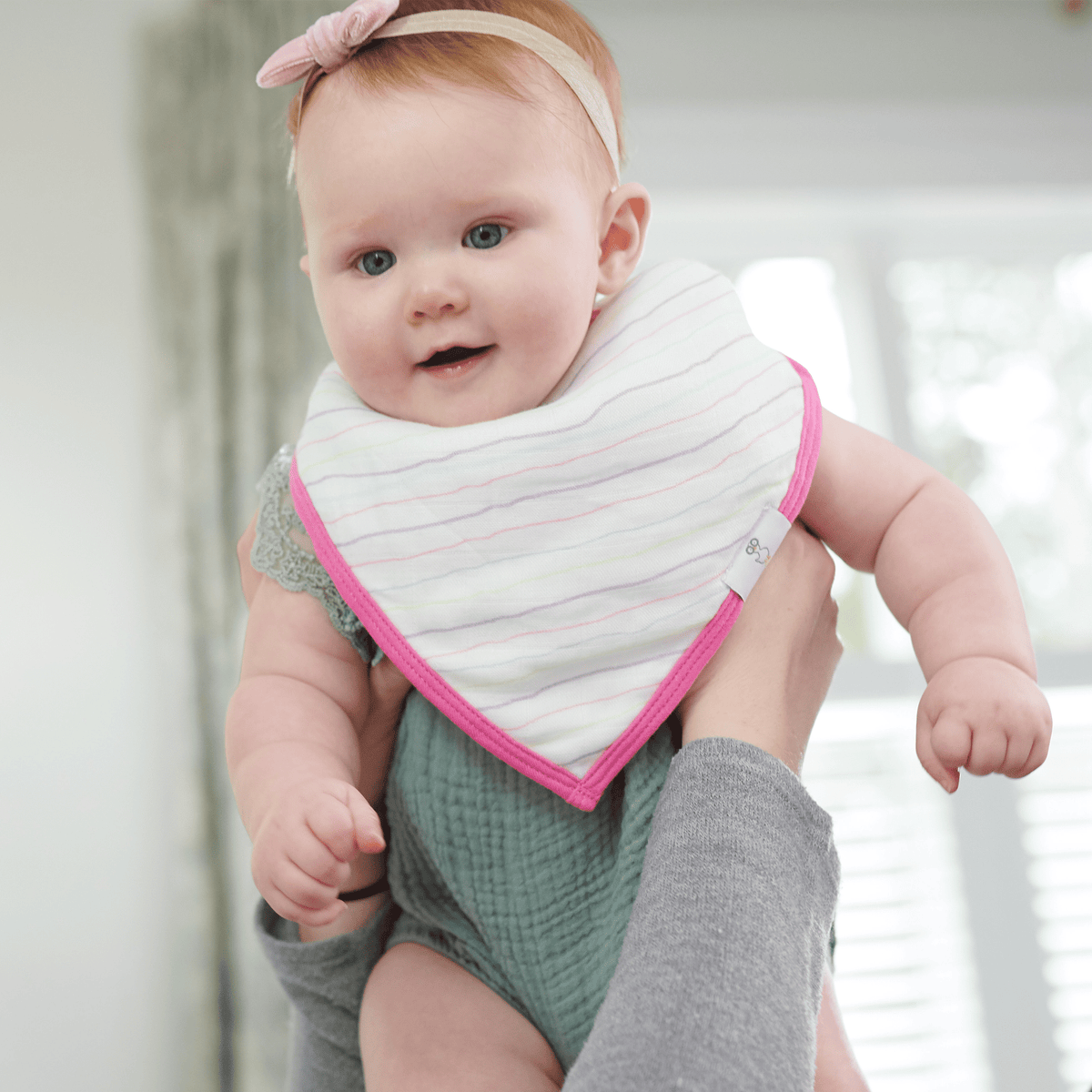 Newborn baby girl wearing white striped baby bibs with pink trim and a pink headband