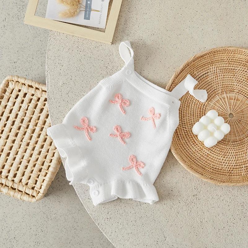 White baby birthday romper with pink bow accents and ruffle hem for infants