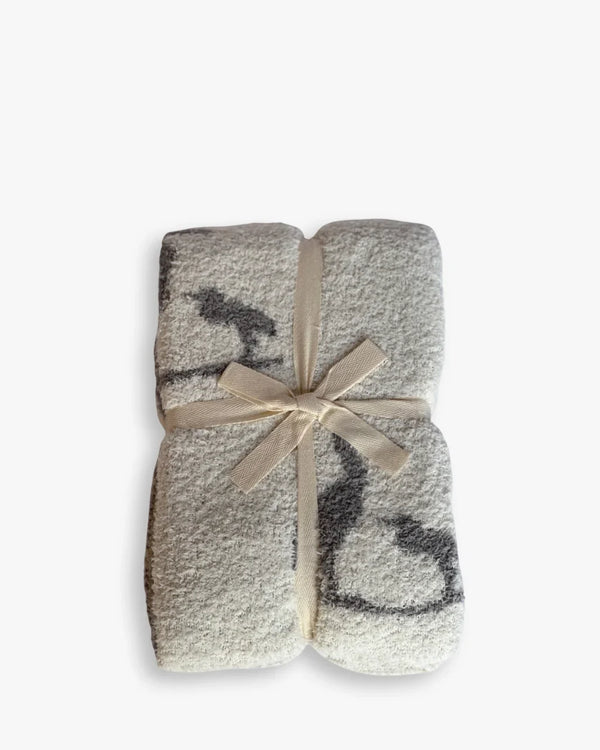 Folded creamy white baby blanket with charcoal heron print, tied with a beige ribbon for coastal elegance and soft comfort.