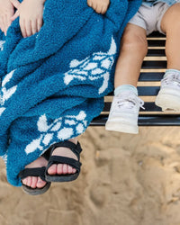 Soft navy blue baby blanket featuring white sea turtle patterns draped over a bench near the sand.