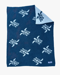 Reversible navy baby blanket featuring white sea turtles gliding across deep blue, with a light blue reverse side.