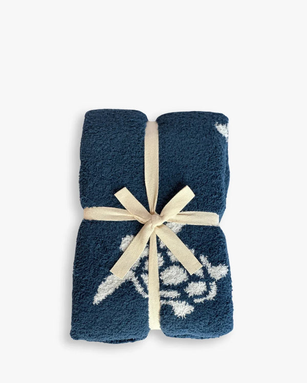 Folded navy blue baby blanket featuring white sea turtle design, tied with cream ribbon for Gulf Coast luxury.