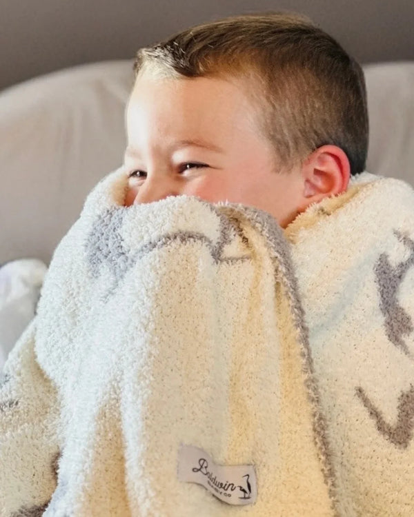 Baby wrapped in creamy white receiving blanket with light charcoal heron print, showcasing plush texture and coastal elegance.