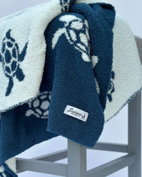 Plush reversible baby blanket featuring white sea turtles on navy and navy turtles on white, showcasing soft coastal texture.