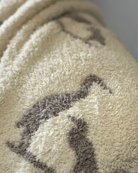 Soft creamy white baby blanket featuring a light charcoal heron print, capturing coastal elegance and luxury comfort.