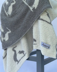 Soft, plush baby blanket featuring a charcoal heron print on creamy white fabric. Coastal elegance with a Baldwin Baby Co tag.