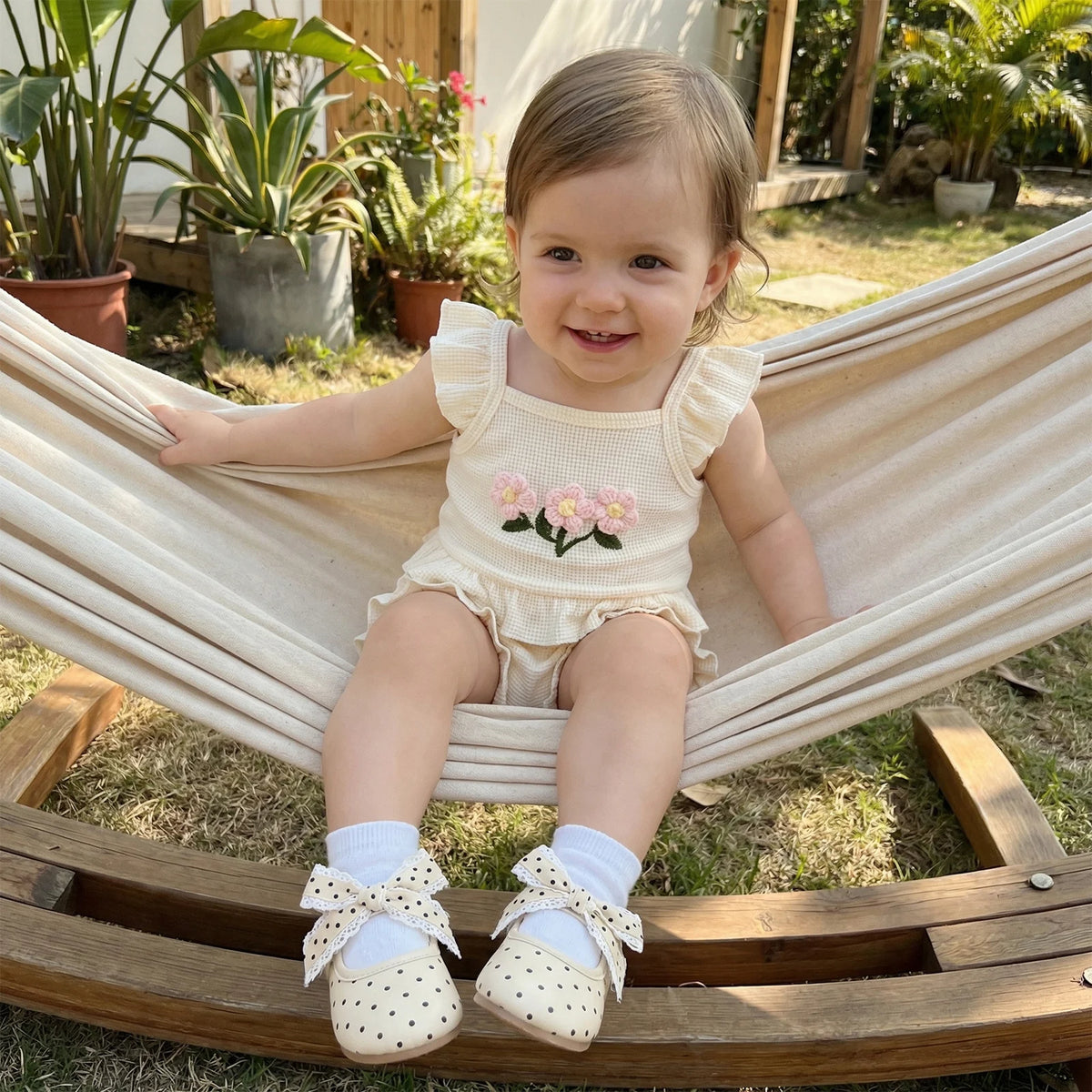 cream baby girl clothes with pink flower embroidery and ruffle sleeves sitting in hammock