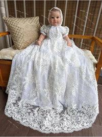 baby wearing white baby christening gown with bonnet sitting on wooden bench with lace details