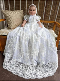 baby wearing white lace baby christening gown with bonnet sitting on wooden bench