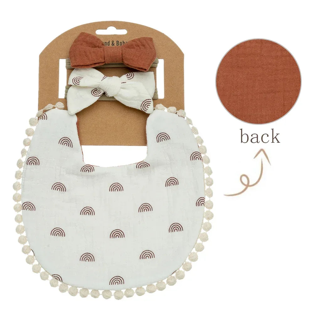 baby flower bib and headband set with white bib featuring brown rainbows and pom pom trim with two coordinating brown and white bows for infants