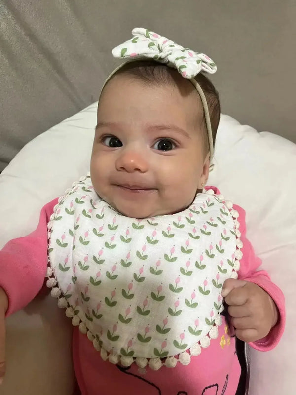 Baby wearing white and pink baby flower bib and headband set with floral pattern smiling and lying down