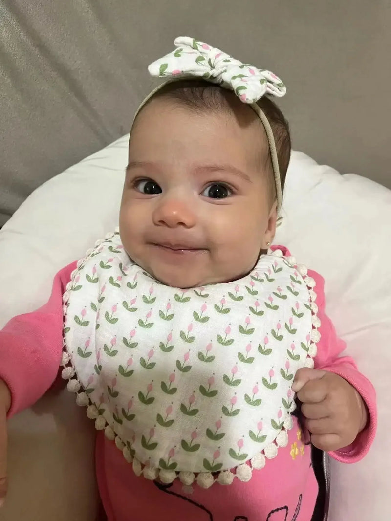 Baby wearing white and pink baby flower bib and headband set with floral pattern smiling and lying down