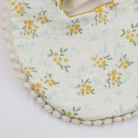 Close-up of white baby flower bib and headband set with yellow floral pattern and lace trim for infants
