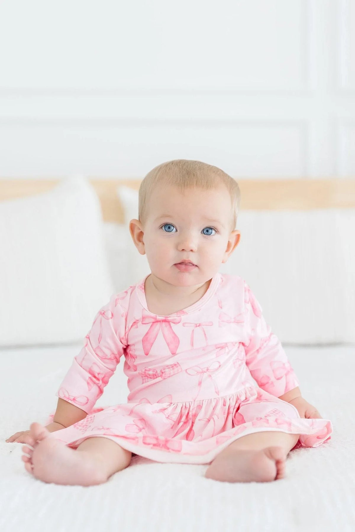 Baby girl wearing pink Mila & Rose Twirl Bodysuit 3/4 sleeve baby girl bow dress sitting on bed