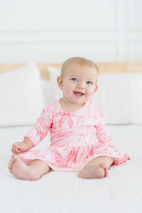 Baby girl wearing pink Mila & Rose twirl bodysuit 3/4 sleeve sitting and smiling on white bed baby girl bow dress