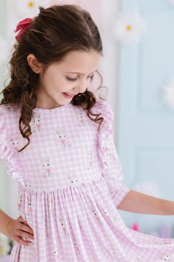 girl wearing pink twirl ruffle dress with baby girl bunny dress pattern smiling and looking down