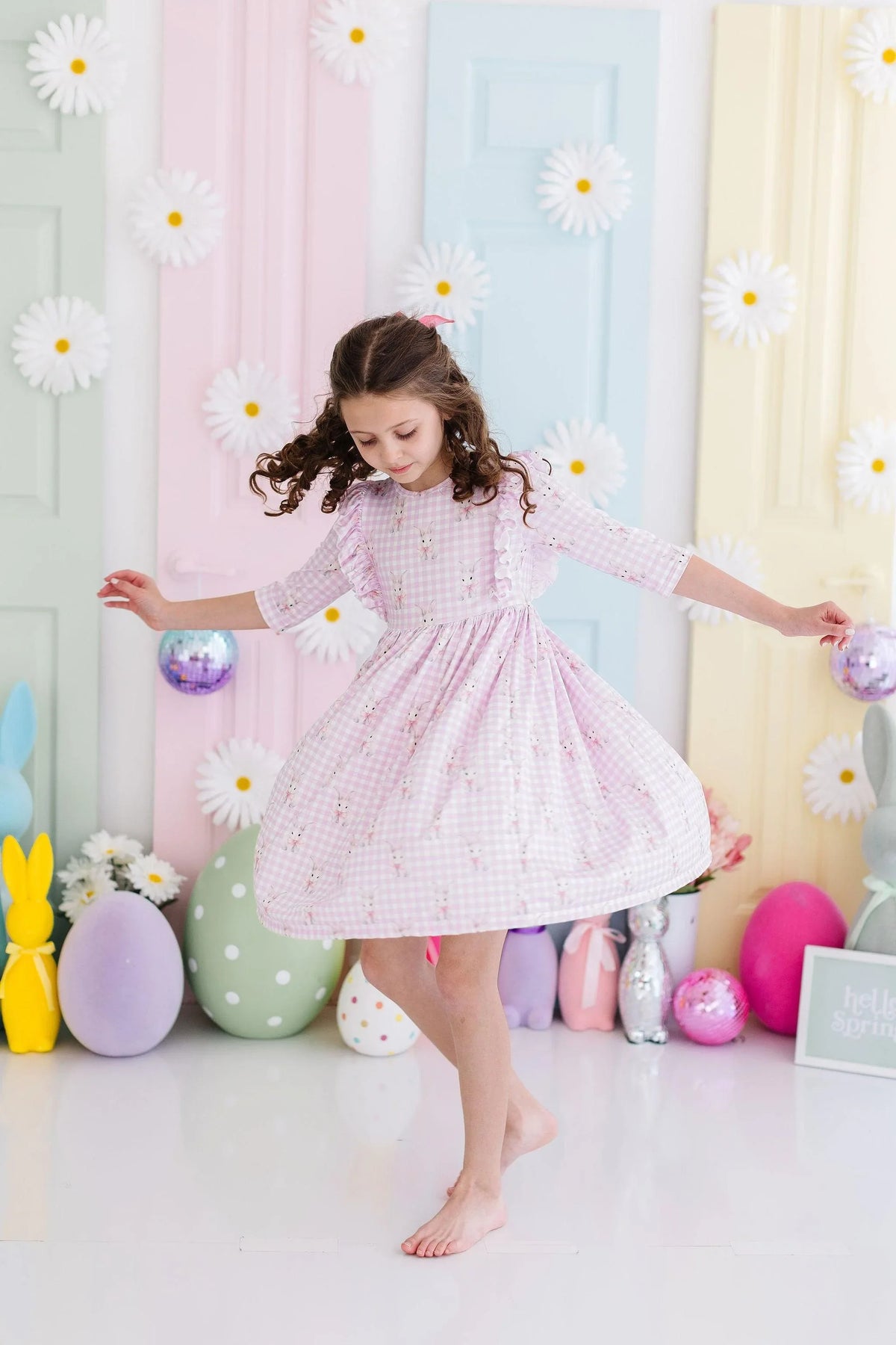 Young girl wearing pink baby girl bunny dress twirling in colorful pastel room with Easter decorations