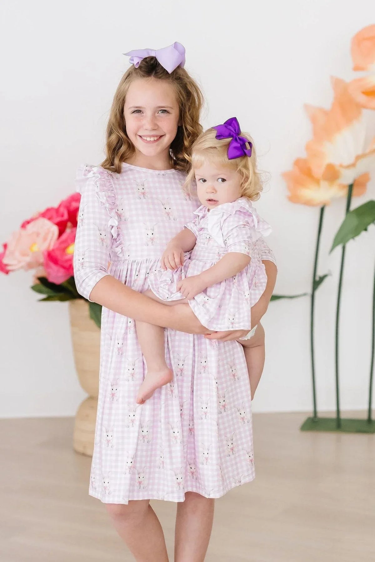 Girl wearing pink twirl ruffle dress holding toddler in baby girl bunny dress with purple bows