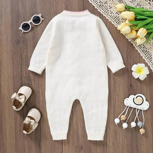 White baby knit romper with flower design made of soft cotton material laid flat with baby shoes and sunglasses