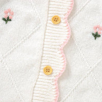 White baby knit romper with flower design featuring pink embroidered flowers and wooden buttons made of soft knit material