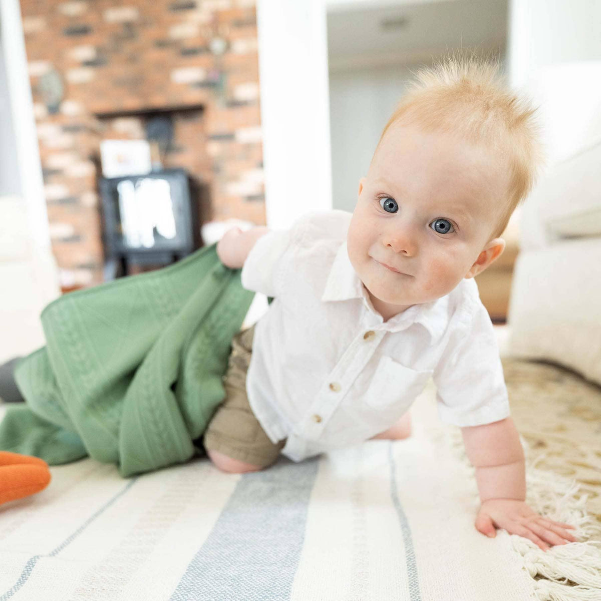 baby boy crawling on rug holding green knit baby blanket from Goosewaddle