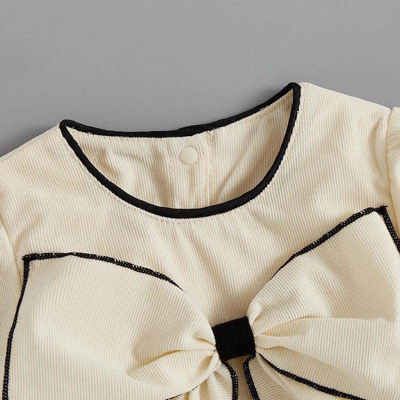 cream baby romper with oversized bow and black trim for infants