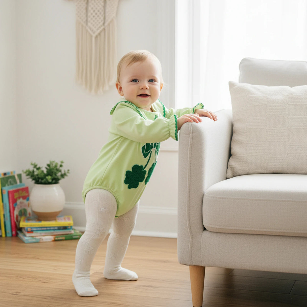 Light green cotton shamrock embroidered baby bubble romper worn by standing baby indoors