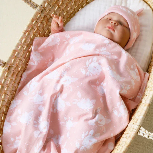 Newborn baby wrapped in pink floral swaddle wrap with matching hat sleeping in woven basket
